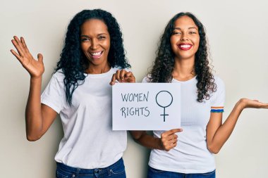 Afrika kökenli Amerikalı anne ve kız ellerinde kadın hakları pankartı mutlu bir gülümsemeyle zaferi kutluyor ve kazanan el kaldırarak ifade ediyor. 