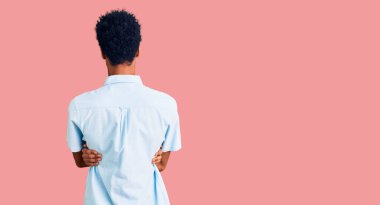 Gündelik giysiler giymiş genç Afro-Amerikan bir adam arkasını dönüp kollarını kavuşturarak başka tarafa bakıyor. 