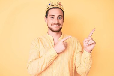 Kral tacını takan yakışıklı genç adam gülümsüyor ve kameraya bakıyor iki eliyle ve parmaklarıyla kenarı işaret ediyor.. 