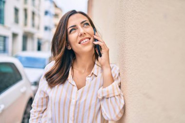 Genç İspanyol kadın gülümsüyor. Şehirdeki akıllı telefondan konuşuyor..