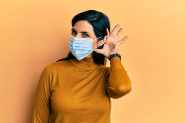 Tıbbi maske takan genç beyaz bir kadın kulağından girip kulağına fısıldayarak dedikoduları ve dedikoduları dinliyor. Sağırlık kavramı. 