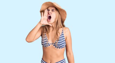 Bikini giyen, şapka takan, el ele verip bağıran genç, güzel sarışın kadın. iletişim konsepti. 