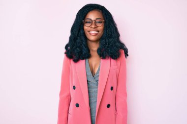 Güzel bir Afrikalı kadın iş ceketi giyiyor ve yüzünde mutlu ve havalı bir gülümsemeyle gözlük takıyor. şanslı kişi. 