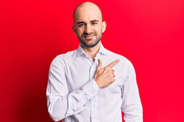 Zarif bir tişört giyen genç ve kel bir adam. Gülümsüyor, elleri ve parmakları yana doğru uzanıyor. 