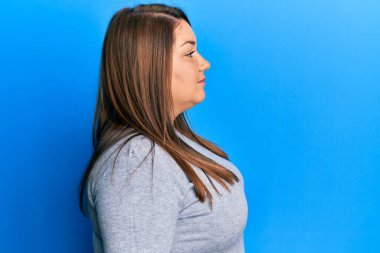 Güzel esmer ve cüsseli bir kadın sıradan kıyafetler giyiyor. Yan tarafa bakıyor, rahat bir poz veriyor. Kendine güvenen bir gülümsemesi var.. 