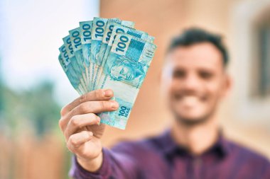 Genç İspanyol gülümseyen adam Brezilya 'nın gerçek paralarını elinde tutuyor..