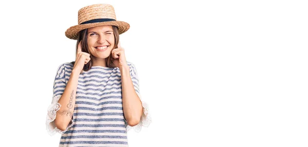 夏の帽子をかぶった美しい白人女性が 大きな音楽のノイズのためにいらいらする表情で指で耳を覆います 聴覚障害の概念 — ストック写真