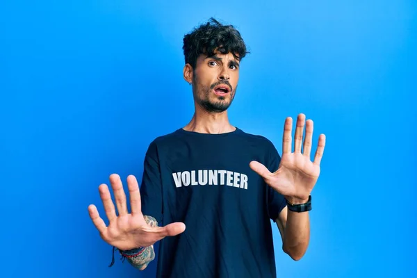 手のひらで停止ジェスチャーを行うボランティアTシャツを身に着けている若いヒスパニック系の男 怒っているとフラストレーション式 — ストック写真