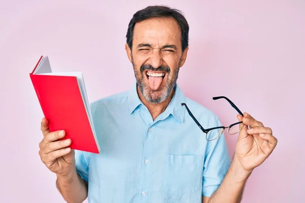 Hombre Hispano Mediana Edad Leyendo Libro Sosteniendo Gafas Sacando Lengua — Foto de Stock