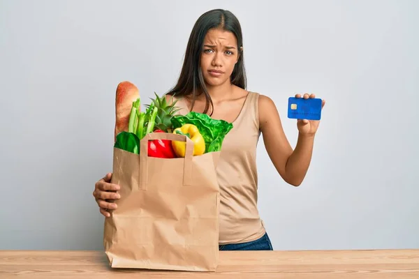 Beautiful Hispanic Woman Holding Groceries Credit Card Skeptic Nervous Frowning — Stock Photo, Image