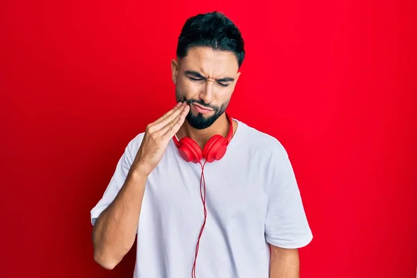 歯の痛みや歯の病気のために痛みを伴う表現で手に触れるヘッドフォンを使用して音楽を聞いてひげを持つ若い男 歯科医 — ストック写真
