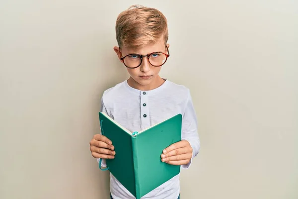 小さな白人の少年が眼鏡をかけて本を読んで懐疑的で緊張し 問題のために動揺して眉をひそめています 否定的な人 — ストック写真