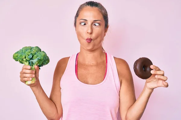 Medelålders Latinamerikansk Kvinna Håller Broccoli Och Choklad Munk Gör Fisk — Stockfoto