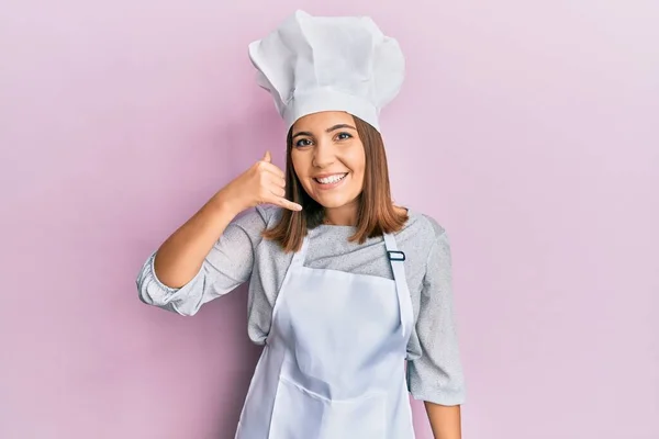 プロの料理人の制服を着て 電話で話すような手や指で携帯電話のジェスチャーを行う笑顔帽子を身に着けている若い美しい女性 コミュニケーションの概念 — ストック写真