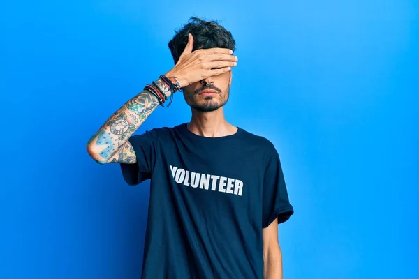 ボランティアのTシャツを着て手で目を覆い 真剣で悲しい顔をしている若いヒスパニック系の男性 目立たず隠し拒否の概念 — ストック写真