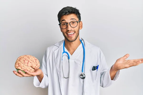 Joven Hombre Guapo Con Abrigo Médico Sosteniendo Cerebro Celebrando Logro — Foto de Stock