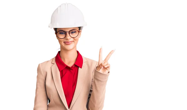 年轻美丽的女人戴着建筑师的硬礼帽 喜形于色地微笑着 在镜头前眨眼示意胜利 第二点 — 图库照片