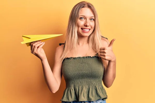 Mladá Blondýna Žena Drží Papírové Letadlo Úsměvem Šťastný Pozitivní Palec — Stock fotografie