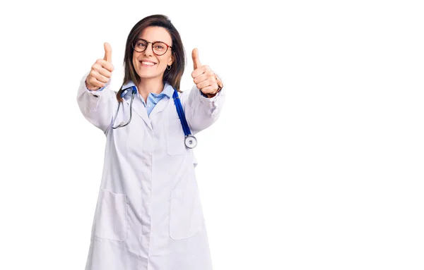 年轻美丽的女人 戴着医生听诊器和眼镜 赞成用手做积极的手势 微笑着竖起大拇指 为成功感到高兴 优胜手势 — 图库照片