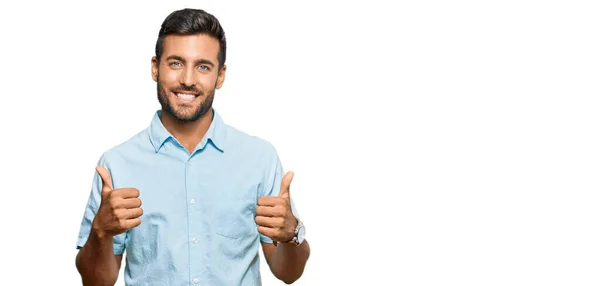 手で積極的なジェスチャーを行うカジュアルな服の成功のサインを身に着けているハンサムなヒスパニック系の男 親指を笑顔と幸せ 陽気な表情と勝者のジェスチャー — ストック写真