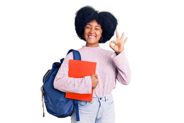 若いですアフリカ系アメリカ人の女の子を着て学生のバックパックを保持本を持っています指でOkサインを行います 笑顔優しいジェスチャー優れたシンボル — ストック写真