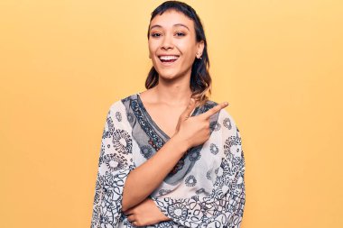 Gündelik kıyafetler giyen, gülümseyen, eli ve parmağı yanda olan genç bir kadın. 