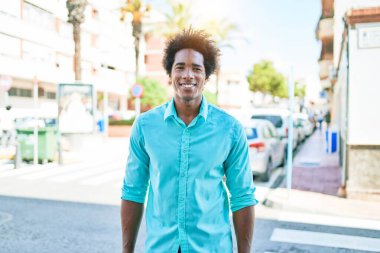 Genç, yakışıklı, Afro-Amerikan bir adam günlük giysiler giyip mutlu gülümsüyor. Yüzünde gülümsemeyle kasaba caddesinde yürürken.