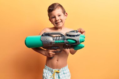 Mayo giyen tatlı sarışın çocuk su tabancası tutuyor gururla bağırıyor, zaferi kutluyor ve başarıyı kollarını kaldırarak kutluyor. 