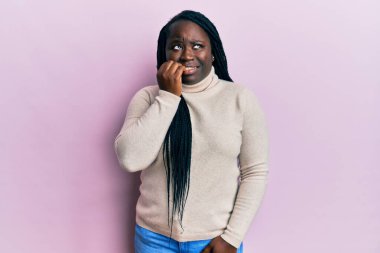 Saçları örgülü, sıradan bir kazak giyen genç siyahi kadın gergin ve gergin görünüyor. Ağzı tırnak yiyen ellerle. anksiyete. 