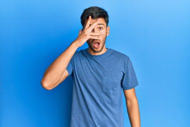 Mavi arka planda sıradan bir tişört giyen genç yakışıklı. Şoka girip yüzünü ve gözlerini eliyle kapatıp parmaklarından korkuyla bakıyor. 