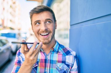 Genç beyaz adam gülümsüyor. Şehirdeki akıllı telefonu kullanarak sesli mesaj gönderiyor..