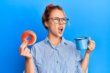 Genç kızıl saçlı kadın elinde çikolatalı çörek ve kahveyle kahvaltı yapıyor kızgın ve öfkeli çığlıklar atıyor öfkeyle bağırıyor, öfkeyle yukarı bakıyor. 