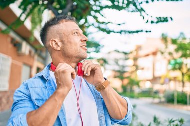 Genç beyaz adam şehirde kulaklık takarak mutlu bir şekilde gülümsüyor..