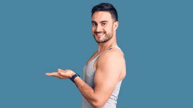 Mayo ve kolsuz tişört giyen genç yakışıklı adam avuçlarını açıp fotokopi alanını gösteriyor, gülümseyerek mutlu bir şekilde gülümsüyor. 