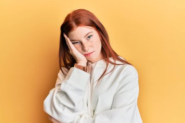 Genç kızıl saçlı kız sıradan bir eşofman üstü giyiyor. Kollarını kavuşturup depresyondan sıkılmış ve yorgun görünüyor.. 