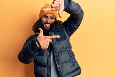 Gündelik kışlık giysiler giyen genç bir Arap gülümseyerek elleri ve parmakları gülen yüzlü bir çerçeve yapıyor. yaratıcılık ve fotoğrafçılık kavramı. 