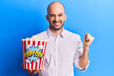 Genç yakışıklı kel adam elinde patlamış mısırla gururla bağırıyor zaferi ve başarıyı kutluyor. 