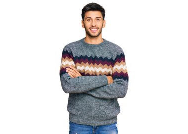 Kış süveteri giyen genç yakışıklı adam kameraya bakarak kollarını kavuşturup gülümsüyor. pozitif kişi. 