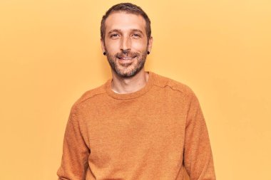 Gündelik kıyafetler giyen yakışıklı genç adam pozitif ve mutlu görünüyor. Duruyor ve gülümsüyor. Kendine güvenen bir gülümsemeyle dişlerini gösteriyor. 