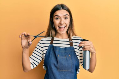 Genç İspanyol kadın kuaför önlüğü giyiyor ve elinde makas var. Çılgınlığı kutluyor ve başarı için hayrete düşüyor. Gözleri açık, heyecanlı çığlıklar atıyor.. 