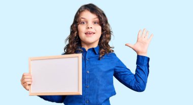 Uzun saçlı tatlı İspanyol çocuk elinde boş beyaz karatahta ile zaferi kutluyor mutlu bir gülümseme ve ellerini kaldırarak kazanan yüz ifadesi. 