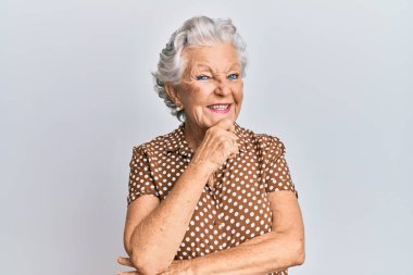 Yaşlı, gri saçlı, sıradan kıyafetler giyen, eli çenesinde soru soran, düşünceli bir kadın. Düşünceli bir yüzle gülümsüyor. şüphe kavramı. 