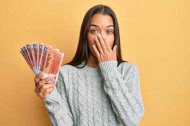 Elinde 100 Norveçli banknot tutan güzel İspanyol kadın ağızlarını eliyle kapatıyor, şaşırmış ve hata yapmaktan korkuyor. şaşırmış ifade 