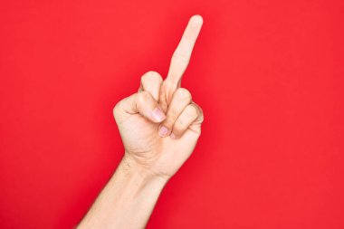 Hand of caucasian young man showing fingers over isolated red background showing provocative and rude gesture doing fuck you symbol with middle finger