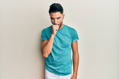 Sakallı genç adam, günlük giysiler giyiyor kendini iyi hissetmiyor ve soğuk algınlığı veya bronşitin belirtisi olarak öksürüyor. sağlık hizmeti kavramı. 