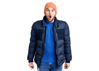 Kışlık giysiler giyen genç yakışıklı adam korkmuş ve ağzı açık kalmış, şaşırmış ve şaşırmış. 