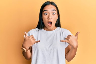Genç Asyalı kadın elleriyle shaka işareti yapıyor. Şaşırmış ve şaşırmış bir ifade, korku ve heyecanlı bir yüz ifadesi var.. 