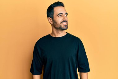 Latin kökenli genç bir adam günlük giysiler giyiyor, rahat bir görünüm takınıyor, doğal bir yüz ifadesi ve kendinden emin bir gülümsemeyle poz veriyor.. 