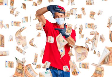 Sarışın, sakallı, teslimat üniforması giyen ve sağlık maskesi takan yakışıklı, elleri ve parmakları mutlu yüzlü bir adam. yaratıcılık ve fotoğrafçılık kavramı.