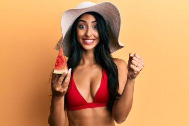 Güzel İspanyol kadın bikini giyiyor, karpuz yiyor gururla bağırıyor, zaferi kutluyor ve kollarını kaldırarak başarıyı kutluyor. 